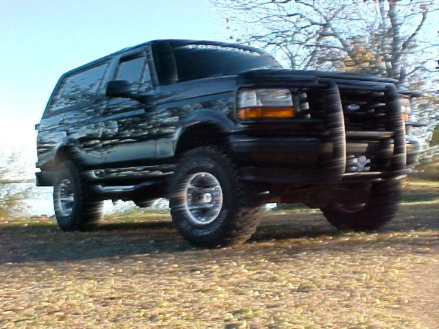 Blurred low-angle shot of lifted black Ford Bronco with brush guard on rough ground