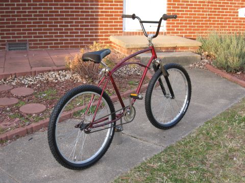1994 Ford Bronco - A red cruiser bicycle with wide tires and high handlebars is parked on a sidewalk in front of a brick house.
