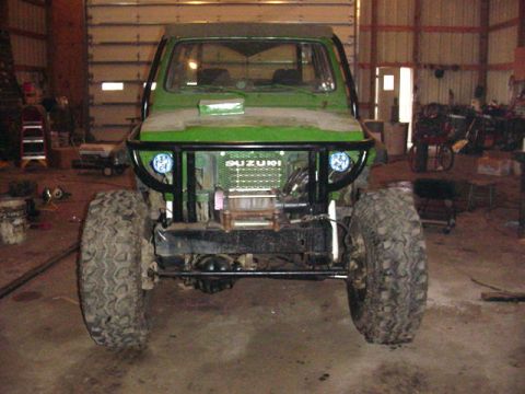 1992 Ford Bronco - A green off-road vehicle with a winch and brush guard is parked inside a garage.