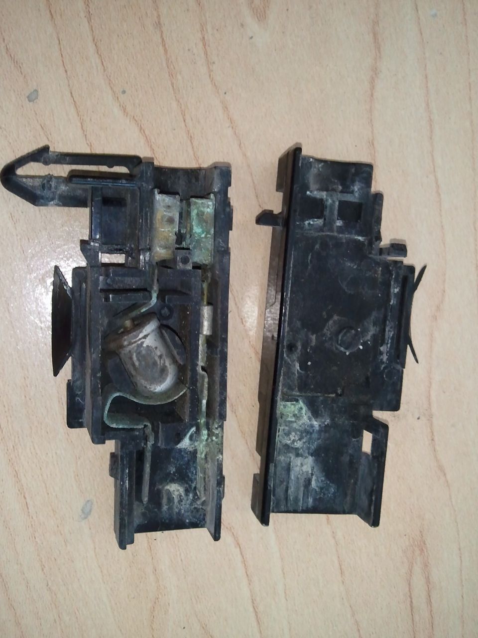 Disassembled black plastic underhood light assembly with corroded metal components on a wooden surface