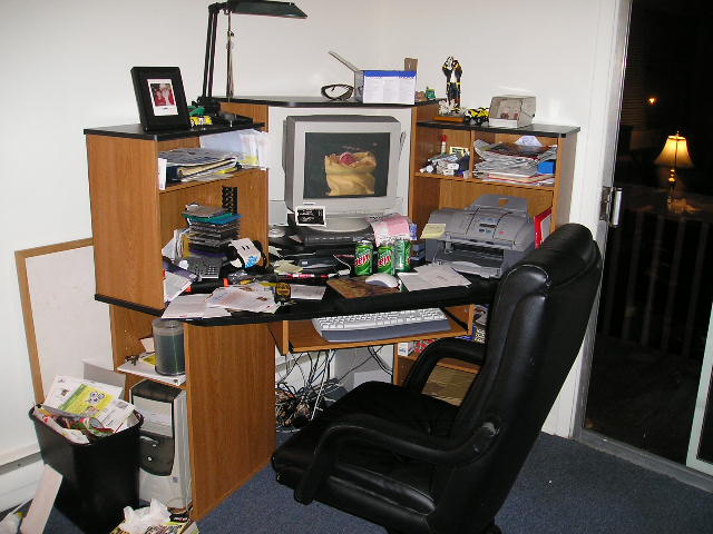 Cluttered desk with computer monitor, keyboard, printer, office chair, and various papers
