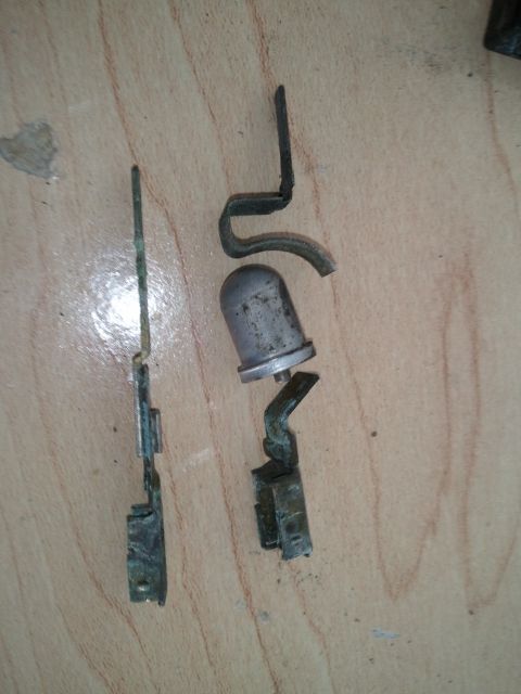 1994 Ford Bronco - Two corroded metal parts, likely from an underhood light assembly, are laid out on a wooden surface.
