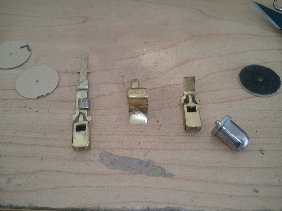 Three brass electrical connectors and a silver bulb on a wooden surface