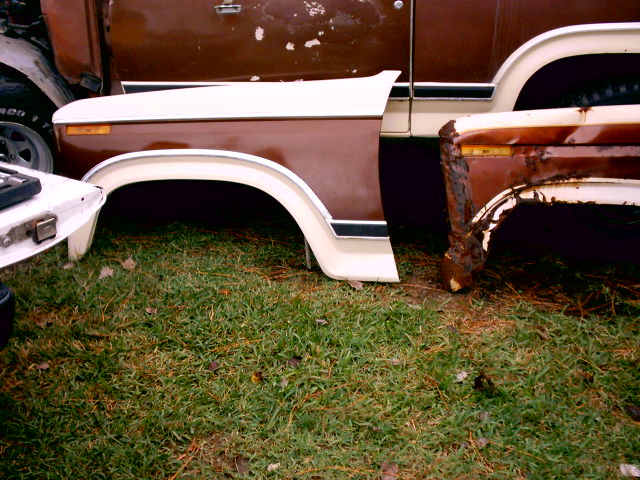Two removed brown and white truck fenders on grass, one rusted through at the corner