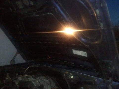 1994 Ford Bronco - The underside of a car's hood is illuminated by a bright light, revealing the engine compartment below.