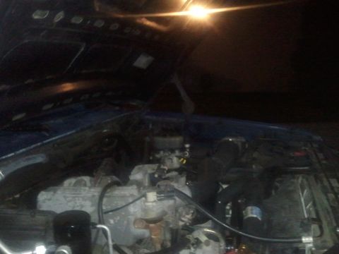 1994 Ford Bronco - The engine bay of a vehicle is visible with the hood open, illuminated by an overhead light.