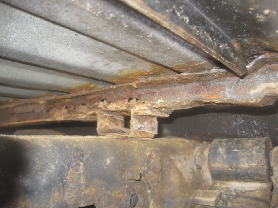 Close-up of heavily rusted frame rails and undercarriage components of a vehicle