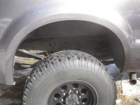 2003 Ford F-350 - Close-up of the rear wheel well and tire of a truck, showing suspension components and exhaust.
