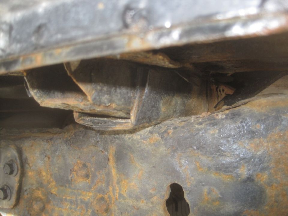 Close-up of heavily rusted metal frame components, likely from the undercarriage of a vehicle