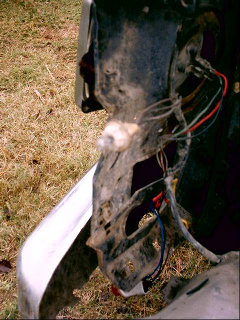 1980 Ford Bronco - Close-up of a truck's exposed front radiator support and headlight mounting bracket with the fender off, showing dirty black sheet metal, a…