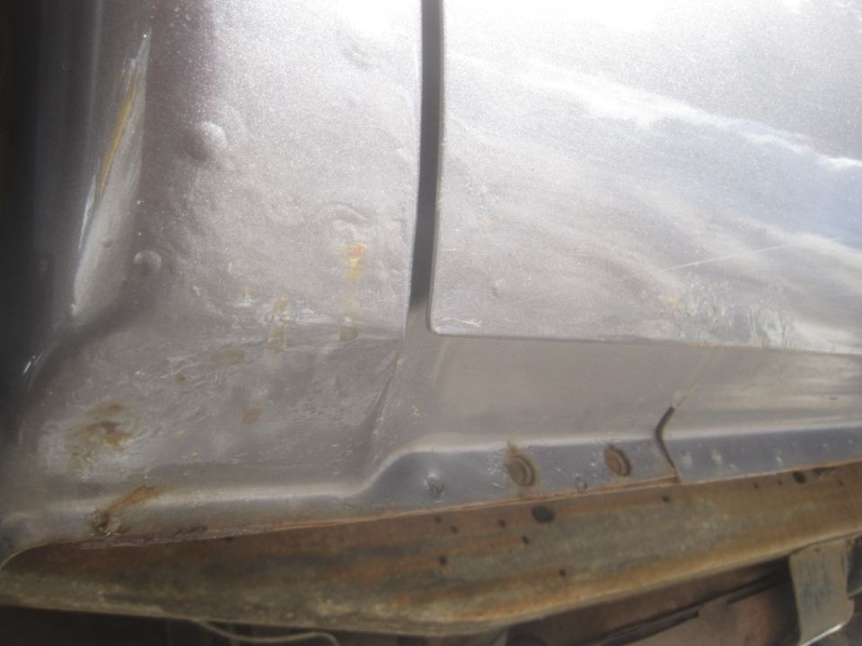 Close-up of a silver truck's lower body panel showing some rust and a seam between panels