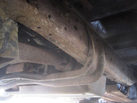 2003 Ford F-350 - The underside of a heavily rusted truck frame shows extensive corrosion and wear on its components.