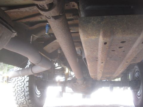2003 Ford F-350 - The underside of a truck reveals its drivetrain, exhaust pipes, and suspension components, showing signs of rust and wear.