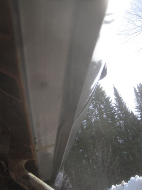 2003 Ford F-350 - A close-up view of a truck's lower body panel reveals signs of wear and rust, with trees visible in the background.