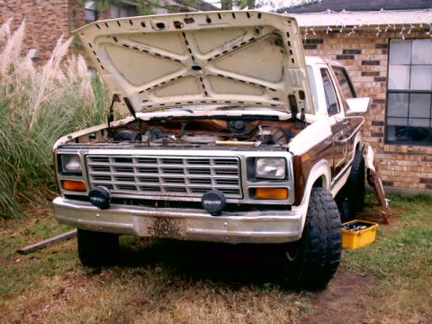 1980 Ford Bronco - Brown and tan full-size Ford Bronco parked on grass beside a brick house with its hood propped wide open, exposing the engine bay, radiator…