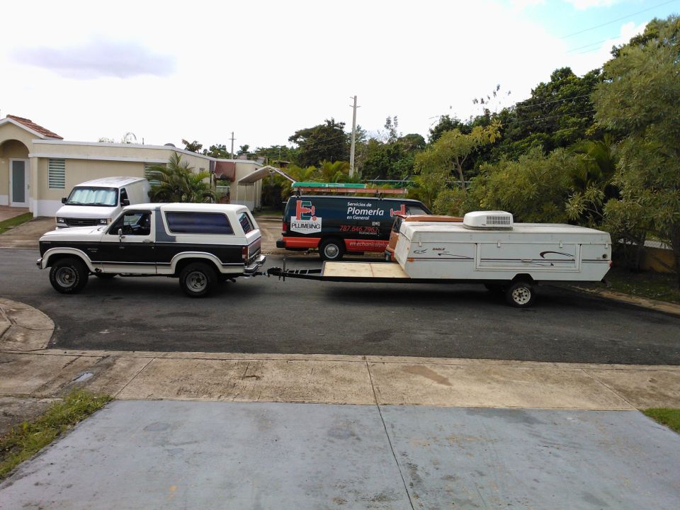 Ford Bronco towing a pop-up camper and a plumbing van is behind it
