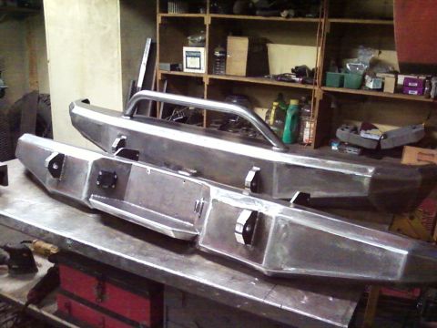 1989 Ford Bronco - Custom fabricated metal bumpers are displayed in a workshop setting, awaiting installation.