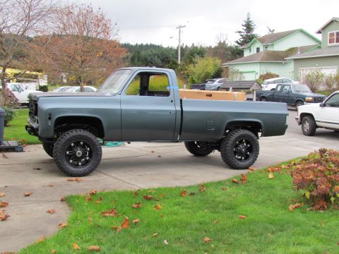 1989 Ford Bronco - A lifted gray pickup truck is parked on a driveway, with other vehicles visible in the background.