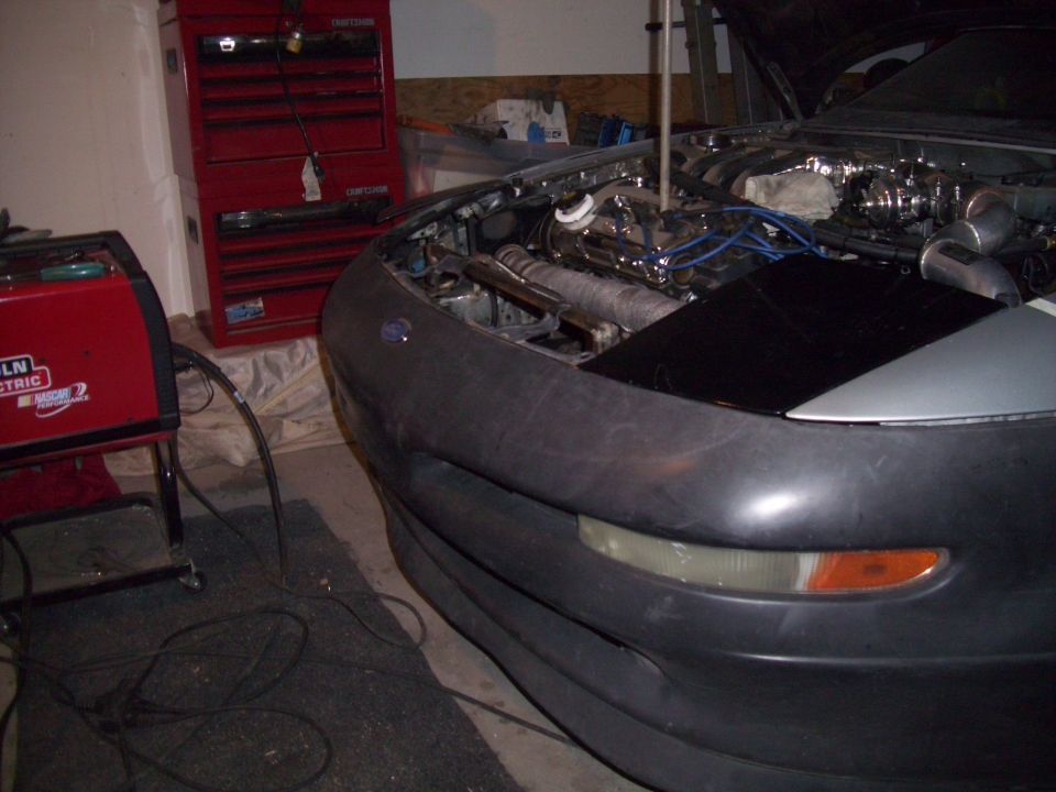 Front view of a 1995 Ford Probe with hood open, showing engine bay and welding equipment nearby
