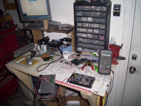 1995 Ford Probe - A cluttered workbench displays a computer setup, various tools, and electronic components, suggesting a workspace for repairs or projects.