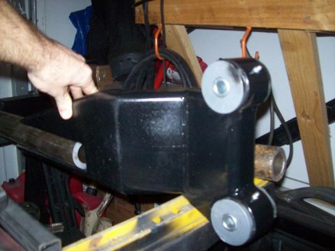 1988 Ford Bronco - A black suspension component with gray bushings is held by a hand in a garage setting.