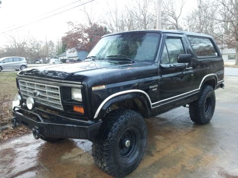 1986 Ford Bronco - Black 1986 Ford Bronco parked on a wet surface, an aftermarket front bumper and lifted suspension.