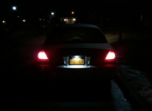 Rear view of a dark sedan at night with its taillights and license plate light illuminated. License plate reads FGR-1408