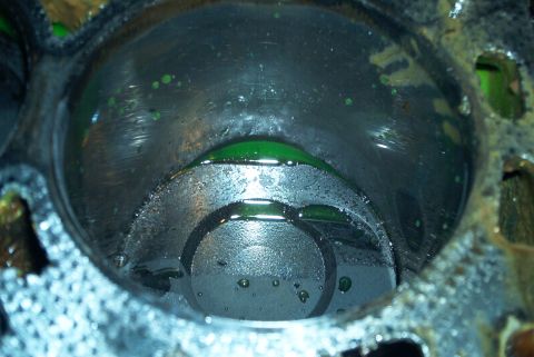 1993 Ford Taurus - Extreme close-up into a single cylinder bore with the head removed, showing green coolant pooled on top of the dished piston and beaded dro…