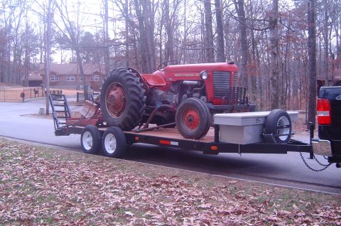 1986 Ford Bronco - A red Massey-Ferguson tractor is loaded onto a trailer, which is being towed by a black pickup truck.
