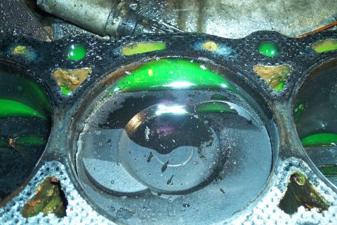 1993 Ford Taurus - Overhead close-up of three cylinder bores on an engine block with the head off, each holding a pool of bright green coolant above the pisto…