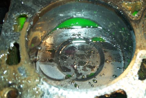 1993 Ford Taurus - Tight overhead shot of one cylinder on an engine block with the head removed, green coolant pooled against the piston crown and droplets cl…