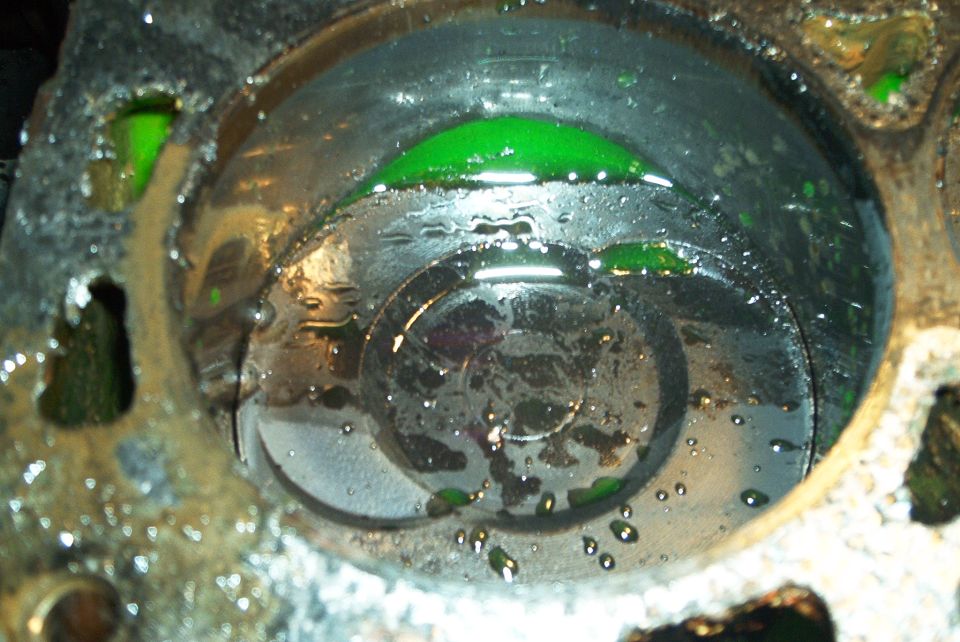 Single cylinder bore with green coolant on the piston and rust-stained block deck
