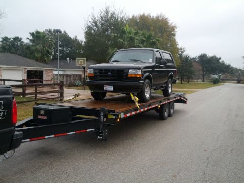 1995 Ford Bronco - A black 1995 Ford Bronco is secured to a flatbed trailer, ready for transport.