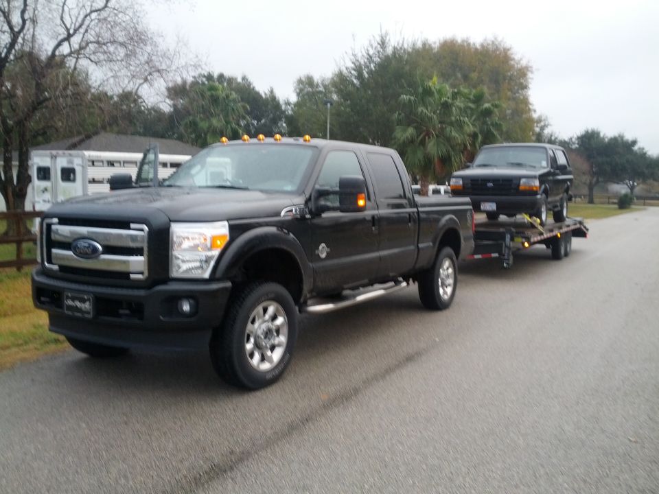 Black 1992 Ford Bronco on a trailer being towed by a black Ford F-series truck