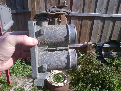 1994 Ford Bronco - A throttle body assembly is held in front of a wooden fence and overgrown weeds.