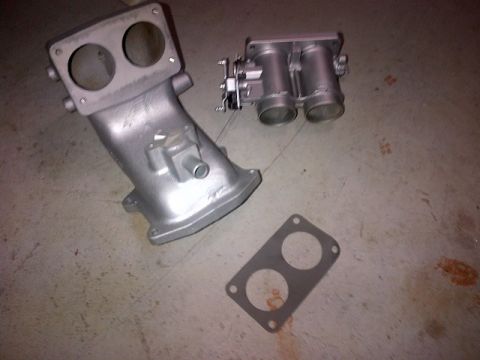 1994 Ford Bronco - Two automotive engine parts, a throttle body and an intake manifold, are laid out on a concrete surface.