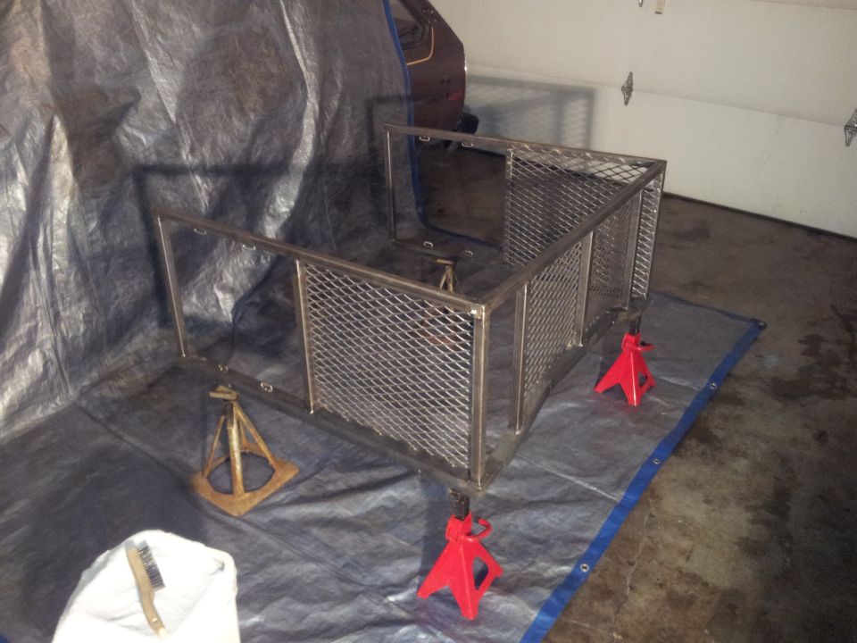 Metal cage frame on jack stands, covered by tarps in a garage