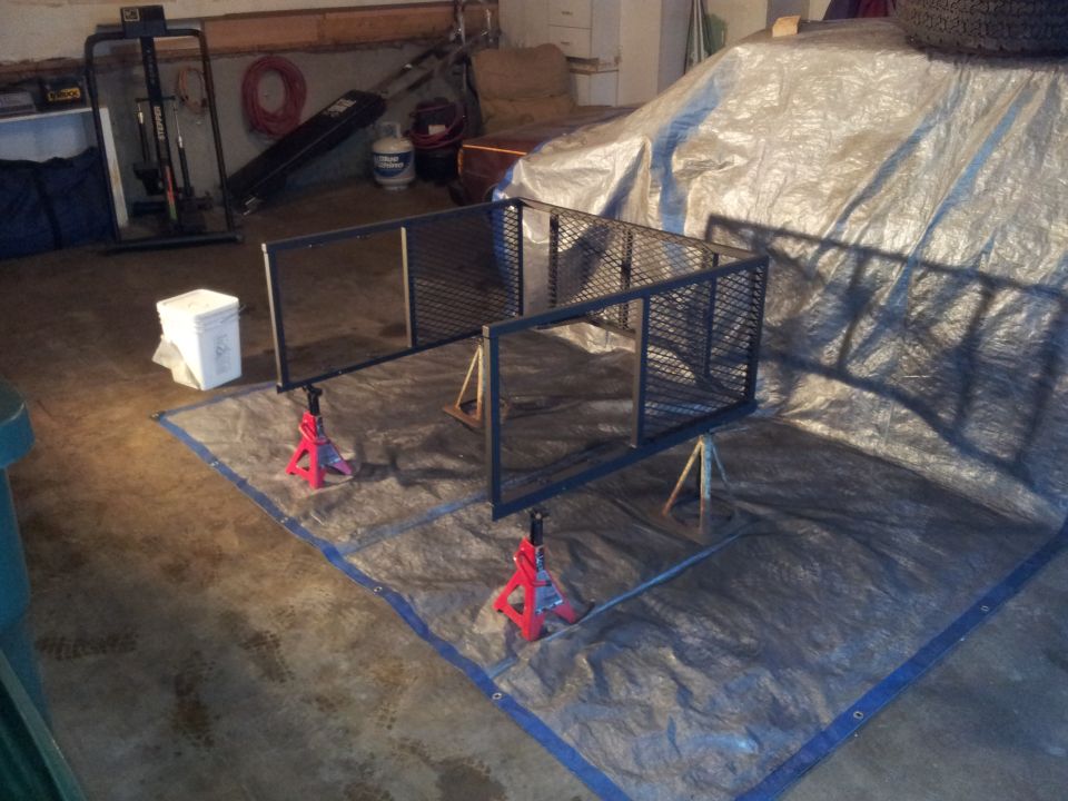 Vehicle covered by a silver tarp, with a tire visible on top, in a garage setting