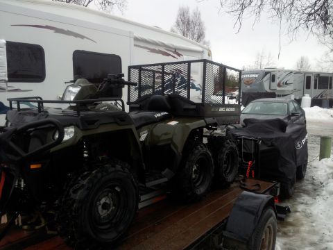 1990 Chevrolet Suburban - An ATV and a covered car are parked on a trailer, with RVs in the background on a cloudy day.