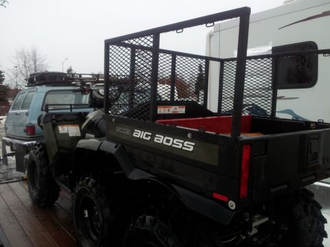1990 Chevrolet Suburban - An ATV with a cargo bed is parked next to a van and a recreational vehicle on a cloudy day.