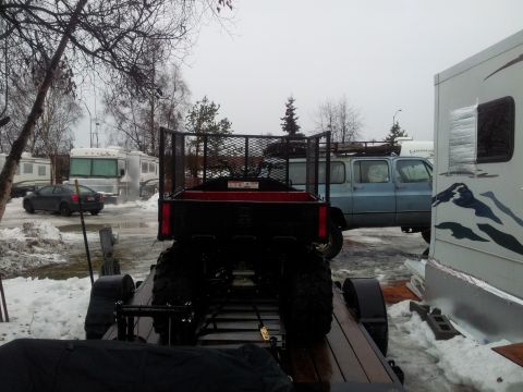 1990 Chevrolet Suburban - Trailer with an ATV is parked near RVs and a blue SUV in a snowy lot.