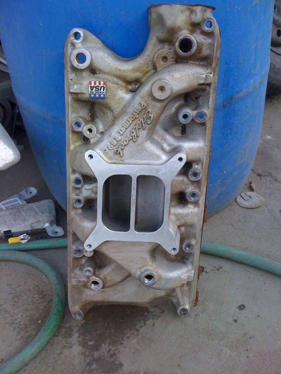 Edelbrock Performer 289 aluminum intake manifold leaning against blue drum on concrete