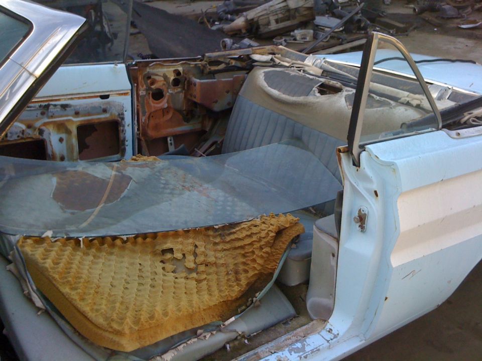 1964 Ford Ranchero interior showing torn door panel, ripped seats, and rusted dashboard. Convertible top is down