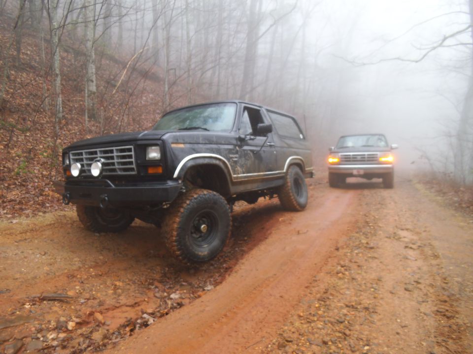 Black lifted 1980s Ford Bronco on a muddy road with another vehicle behind