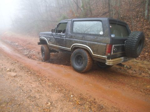 1986 Ford Bronco - This 1986 Ford Bronco is navigating a wet, muddy trail through a forest.