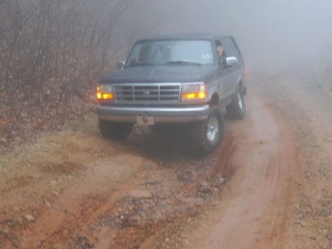 1986 Ford Bronco - A Ford Bronco navigates a foggy, muddy road.