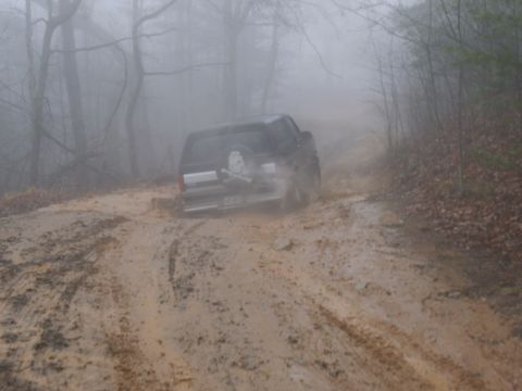 1986 Ford Bronco - A 1986 Ford Bronco navigates a challenging muddy path in a foggy, wooded area.