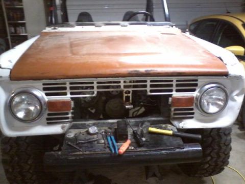 1970 Ford Bronco - The front of a classic Ford Bronco is shown with the hood up, revealing the engine and tools on the bumper.