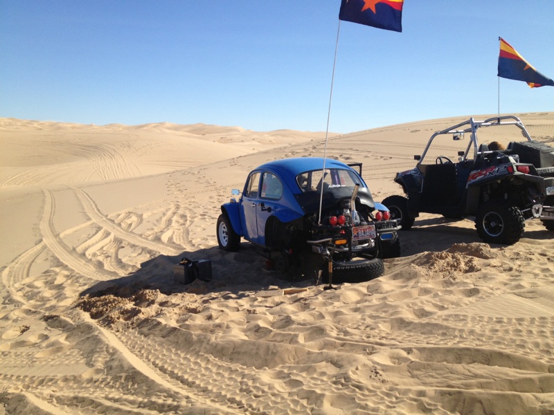 blue VW Beetle with engine exposed, parked in sand dunes next to a side-by-side ATV