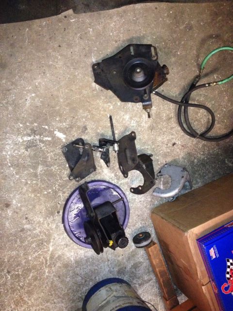 1994 Ford Bronco - Assorted vehicle components, including a power steering pump, are laid out on a concrete surface.